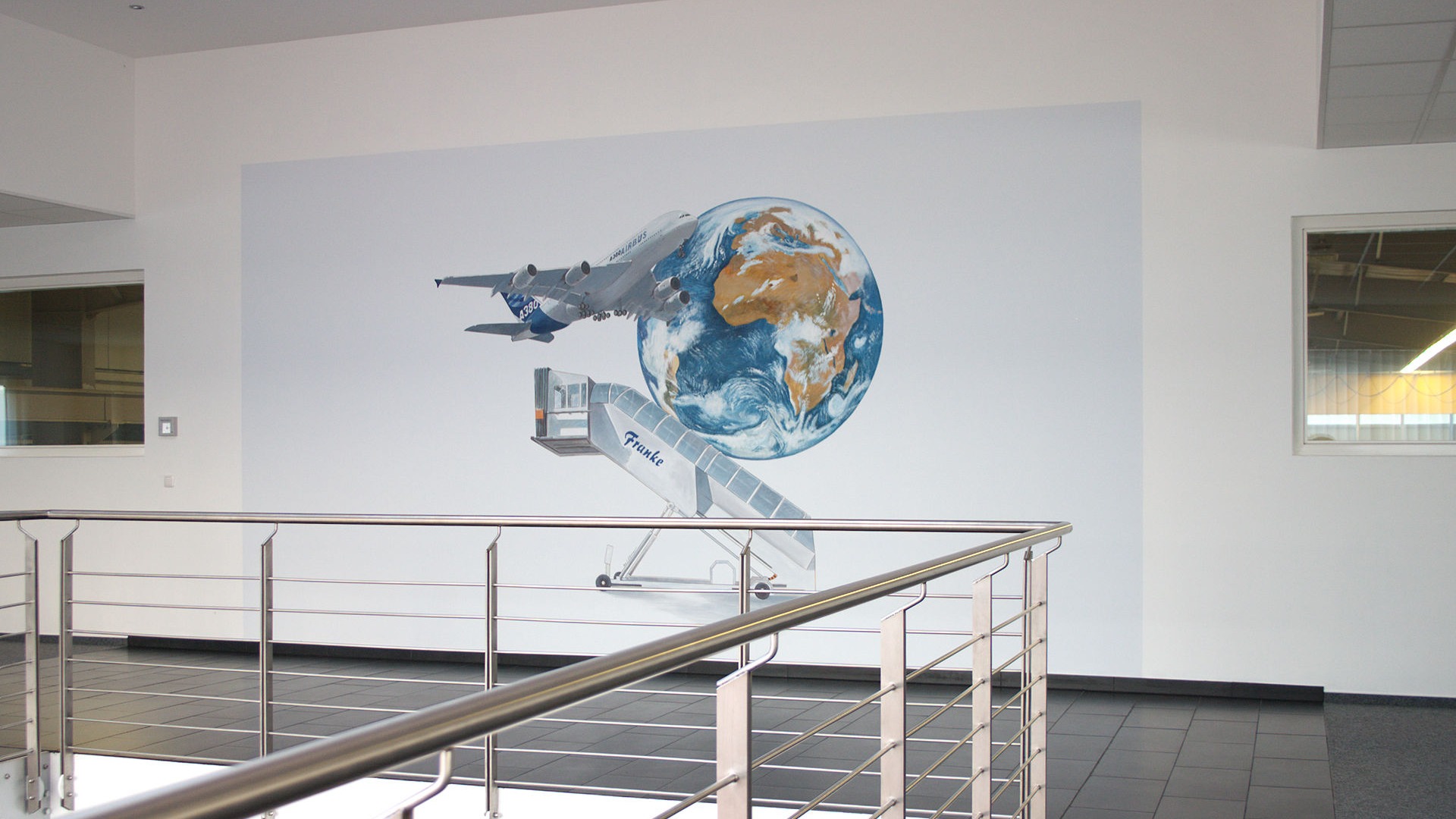 FRANKE ENGINEERING GMBH in Neustadt-Glewe. Hier wurde Kunst im Unternehmen in Form einer Wandmalerei ausgeführt. Die Element Flugzeug, Erdkugel und Rampe symbolisieren die Kooperation mit der Flugzeugindustrie. 